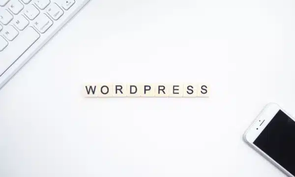 ما الذي يميز wordpress عن غيره من طرق بناء المواقع الإلكترونية ؟ 3 تهجئة كلمة "WORDPRESS" بمربعات حروف على مكتب أبيض مع لوحة مفاتيح وهاتف.