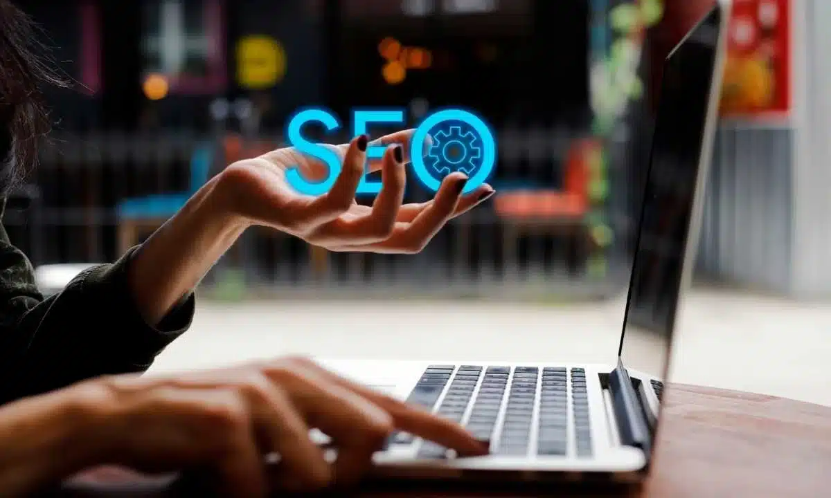 يد تمد نحو كلمة SEO متوهجة فوق لوحة مفاتيح حاسوب محمول.
